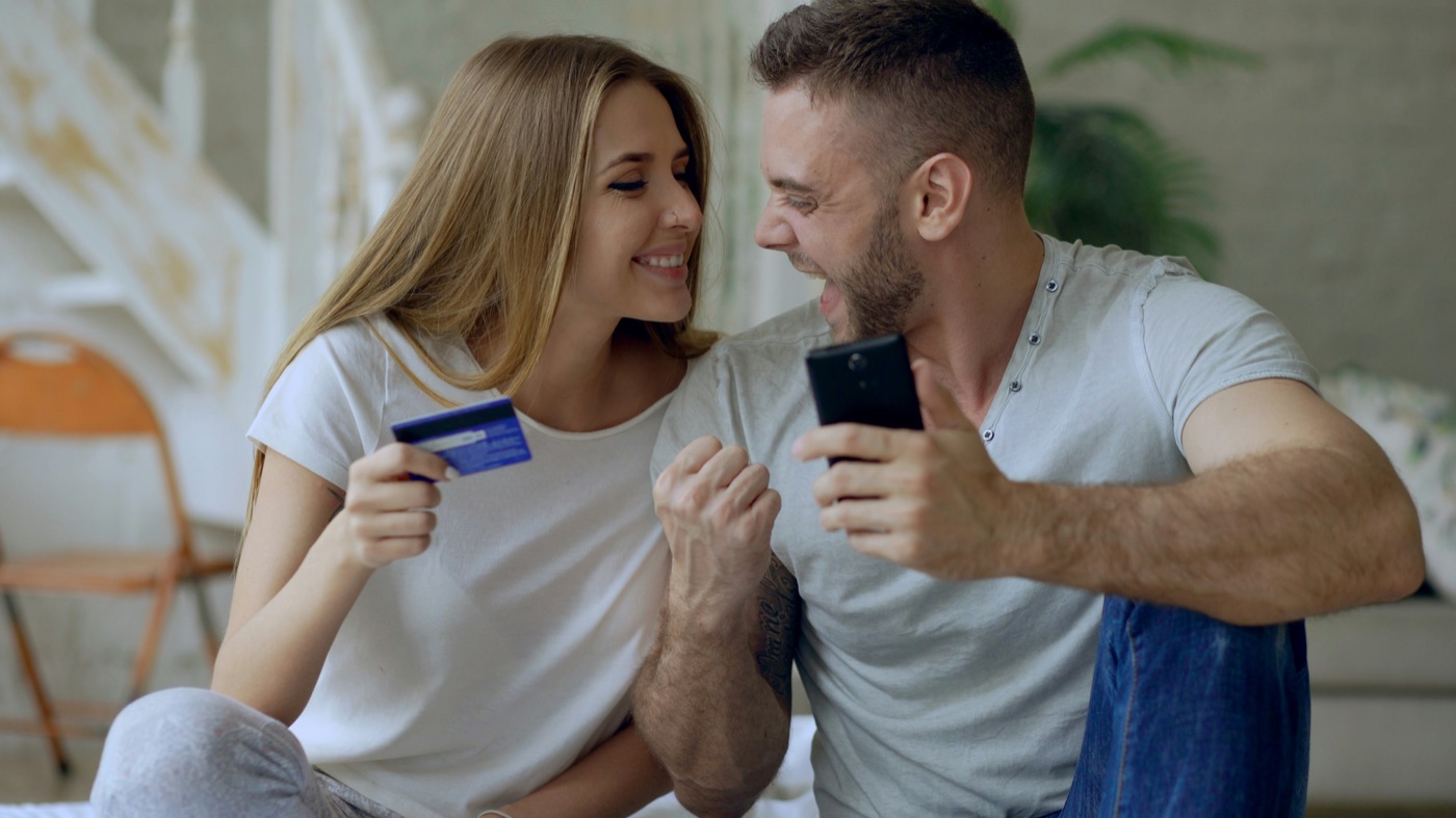 Casal feliz usando o celular e o cartão